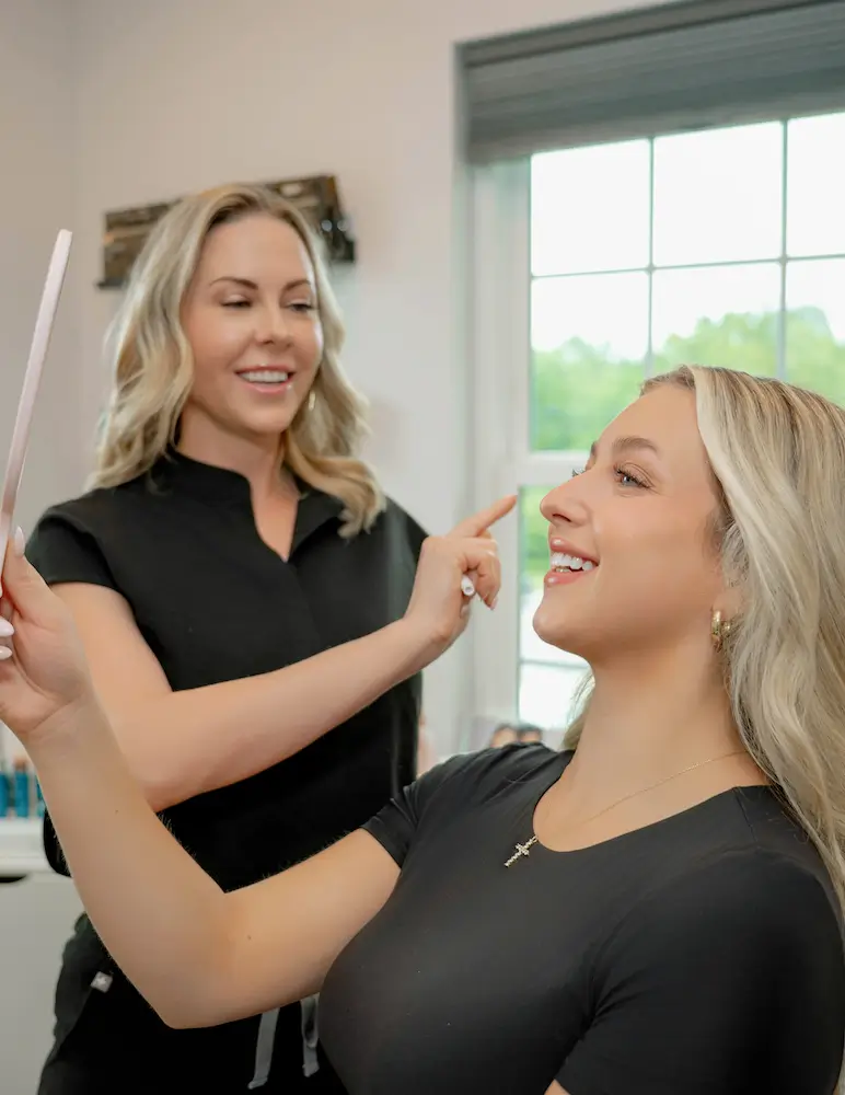 Beauty provider consulting with a client while the client looks into a hand mirror.